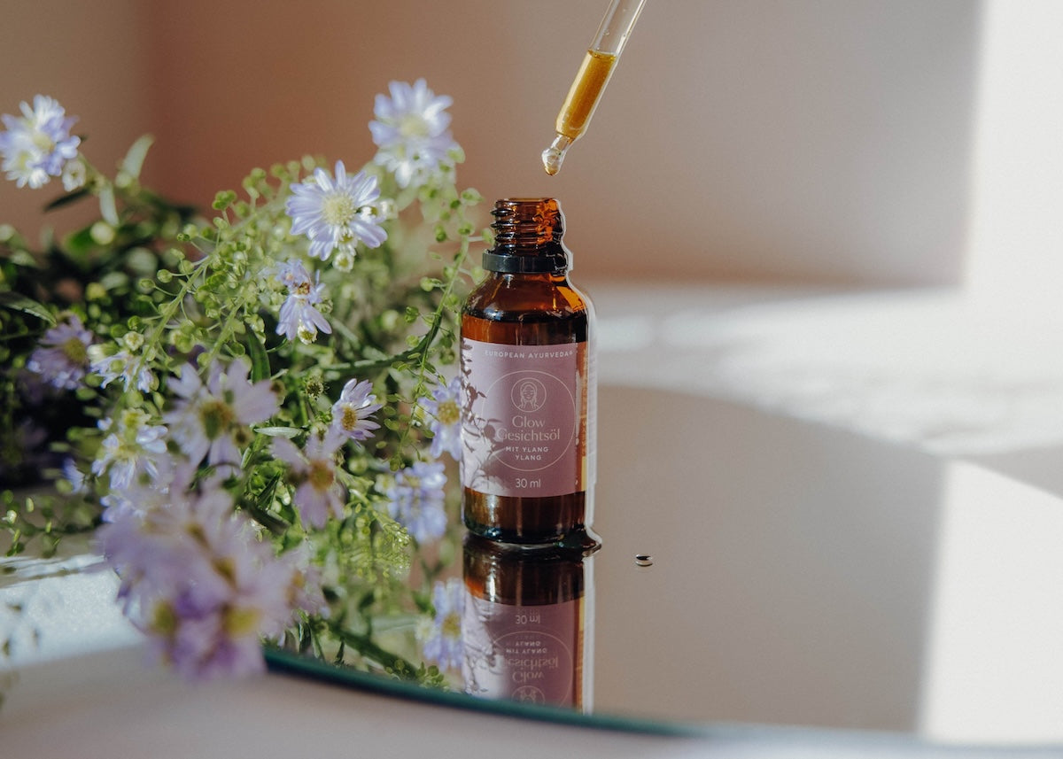 Hand hält eine Flasche Glow Gesichtsöl mit natürlichem Ayurveda-Öl für intensive Gesichtspflege und strahlende Haut.