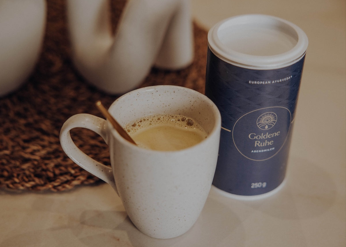 Tasse mit Goldene Ruhe Abendmilch neben der Produktdose – ayurvedisches Abendgetränk für Entspannung und Vata Balance.